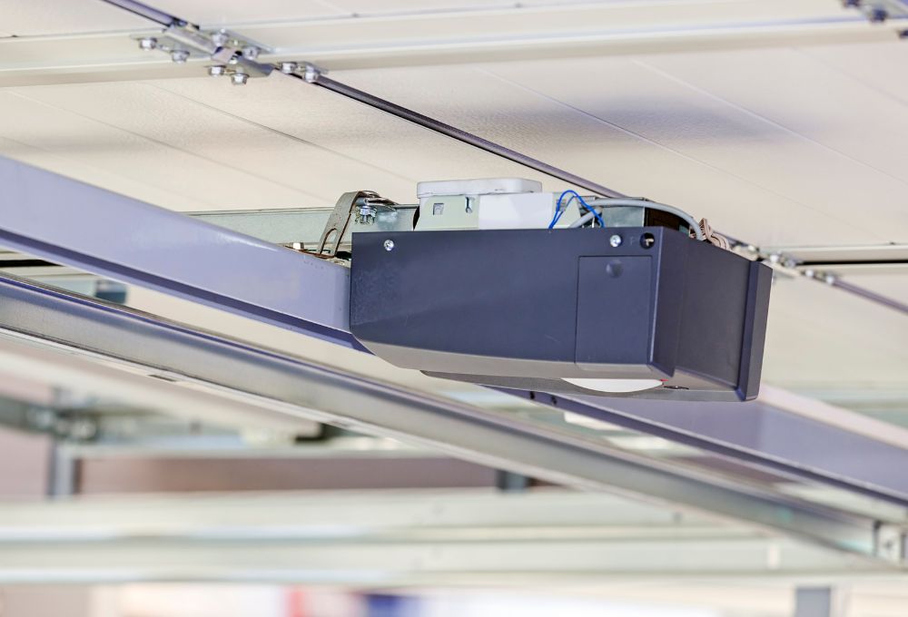 Close-up of a blue garage door opener motor mounted on the ceiling track of a garage.